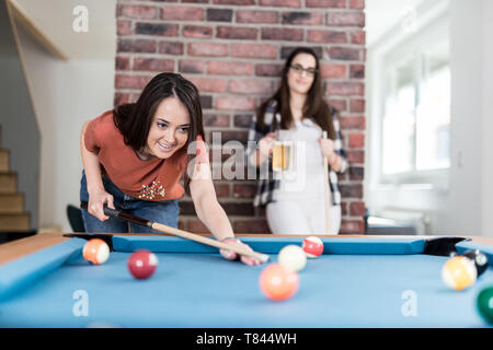 Two female students playing billiard game and drinking beer. Stock Photo