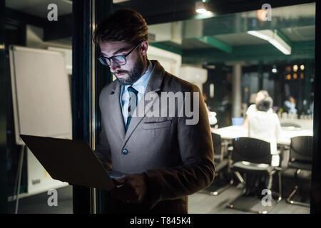 Mid adult businessman looking laptop on office balcony at night