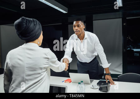 Businessman and woman shaking hands over conference table Stock Photo