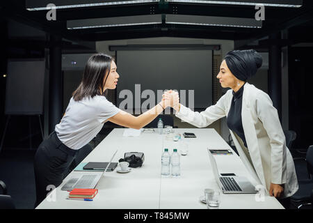 Businesswomen shaking hands over conference table Stock Photo