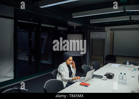 Businesswoman at conference table typing on laptop Stock Photo