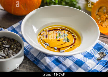 Pumpkin cream soup with seeds and parsley on kitchen table Stock Photo