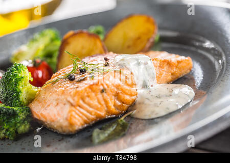 Roasted salmon fillet broccoli tomatoes and fried potatoes with dill cream sauce Stock Photo