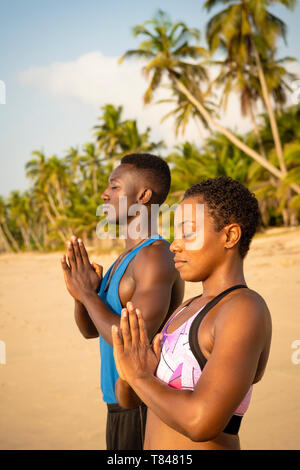 Couple practising yoga on beach Stock Photo