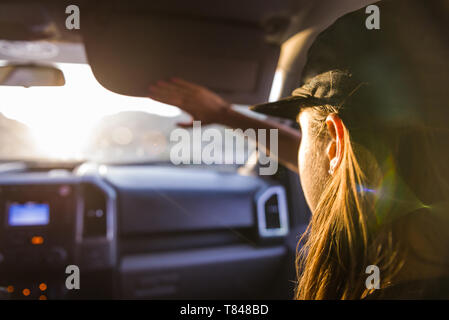 Woman passenger in front seat of car shielding eyes from sunlight, over shoulder view Stock Photo
