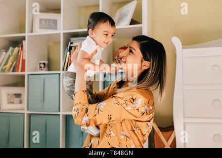 Mother holding up baby son in nursery Stock Photo
