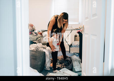 Girl getting dressed with mother in laundry room Stock Photo