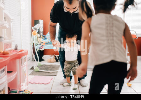Girl in front of father walking baby brother in kitchen Stock Photo