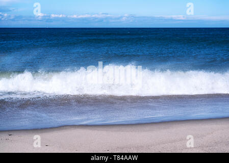 Waves from the Atlantic Ocean crashing onto the beaches of the Cape Cod National Seashore in Truro Massachusetts on a sunny blue sky day. Stock Photo