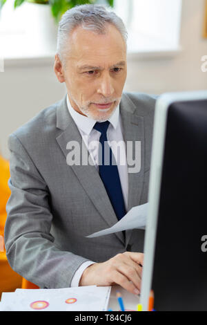 Interested good-looking businessman in black ties attentively looking on the screen Stock Photo