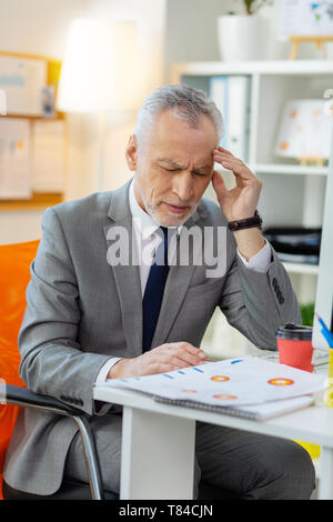 Senior miserable man having extreme headache at work Stock Photo
