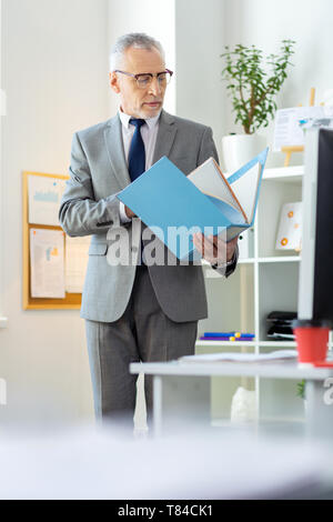 Focused busy old boss in clear glasses inspecting documents Stock Photo