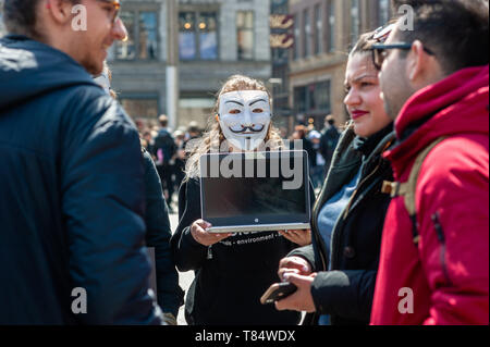 Amsterdam, North Holland, Netherlands. 11th May, 2019. A female activist seen holding a laptop while wearing a Guy Fawkes mask during the demonstration.Hundreds of activists gathered at the Dam square in the center of Amsterdam to participate in The Cube of Truth. Anonymous for the Voiceless hosted a 24-hour Cube of Truth in Dam Square, Amsterdam. The Cube of Truth is a peaceful static demonstration similar to an art performance. This demonstration operates in a structured manner that triggers curiosity and interest from the public; the activists attempt to lead bystanders to a vegan conclusi Stock Photo