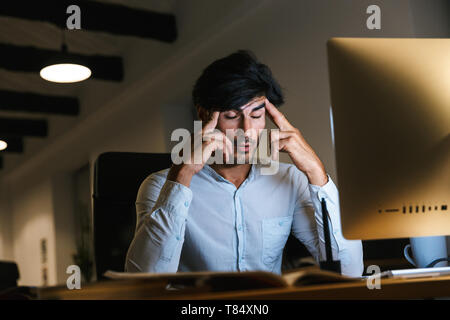 Portrait of a confident concentrated businessman working at the office late at night, having a headache Stock Photo