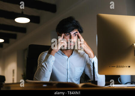 Portrait of a confident concentrated businessman working at the office late at night, having a headache Stock Photo
