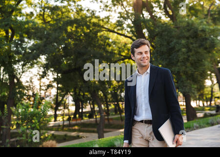 Confident business man walking outdoors, carrying a laptop Stock Photo