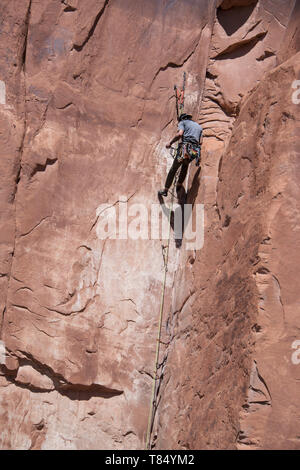 Rock climber man free climbing solo up handholds and footholds on red sandstone cliffs to set pitons and ropes in Moab, Utah, USA, May 7, 2019 Stock Photo