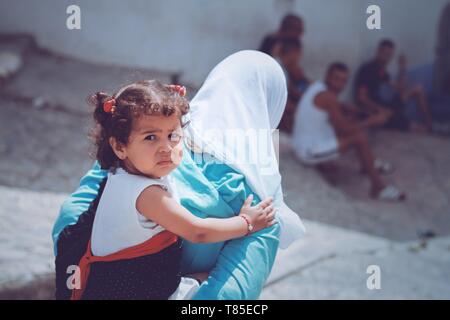 a Muslim woman in white hijab holding her cute little daughter on her back while walking in the streets  Casablanca, Morocco Sep, 14th 2017 Stock Photo