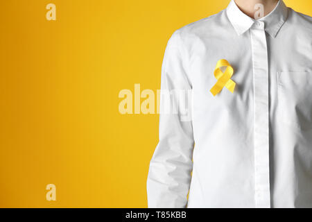 Woman with yellow ribbon against color background. Cancer awareness concept Stock Photo
