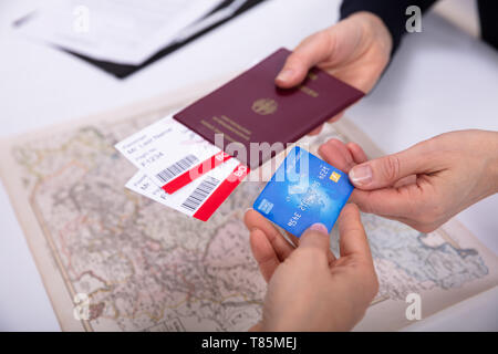 People's Hand Holding Passport And Boarding Pass Ticket With ATM Card Over World Map Stock Photo