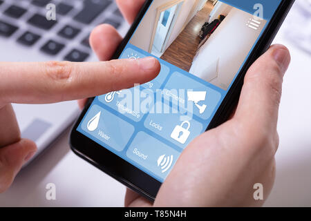 Close-up Of A Businessman's Hand Using Home Security System On Mobile Phone Stock Photo