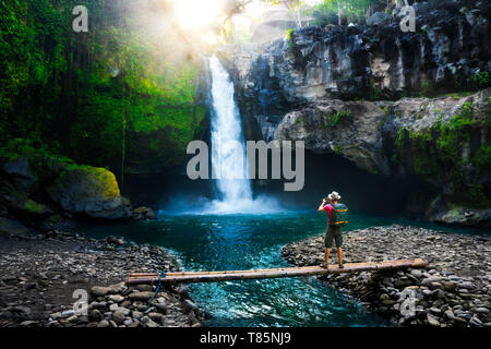 Active lifestyle and Travel concept: Travel backpacker with camera in hand make photo at sunrise amazing waterfall hidden in tropical jungle. Stock Photo