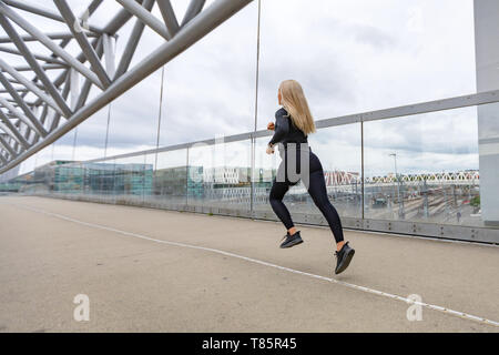 Fast running sporty woman in black workout outfit in modern city environment Stock Photo