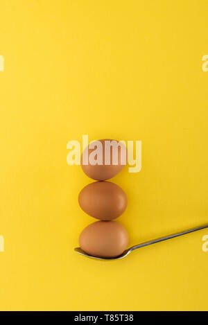 three brown chicken eggs on spoon on yellow background Stock Photo
