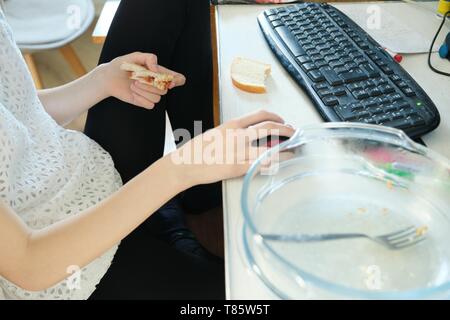Kyiv UA, 26-04-2019. Teenager girl sitting at home near the computer is eating dinner, playing computer game. Stock Photo