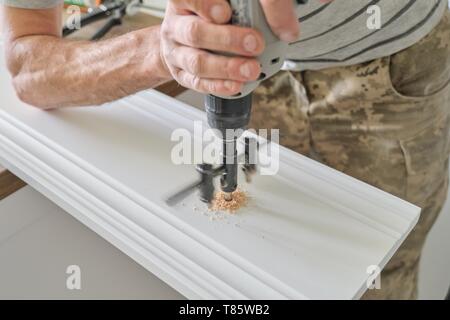 Close-up of carpenters hand using professional woodworking electric tools when working with wood. Male carving hole in wooden panel board, carpentry, 