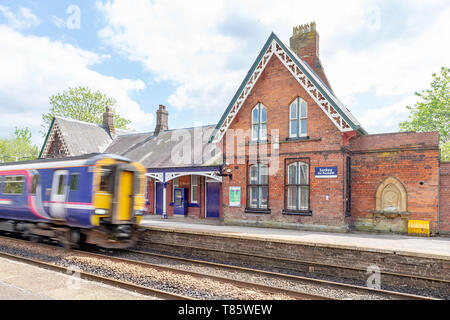 Platform and buildings of Sankey for Penketh Railway Station, West Warrington, Cheshire, England with speeding train passing through Stock Photo