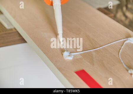 Carpenter male using construction glue when working with wooden white painted board, closeup, carpentry, woodwork, profession, people. Stock Photo