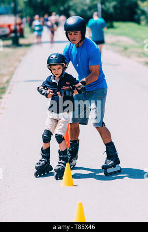 Grandfather teaching grandson to roller skate Stock Photo