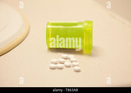 A handful of white pills on a counter in the bathroom with a bottle Stock Photo