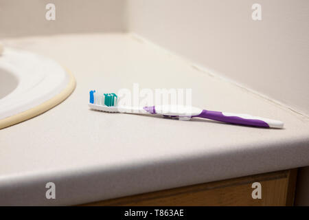 A purple and white toothbrush is on the bathroom counter at home Stock Photo