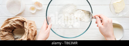 panoramic shot of woman with scoop putting flour in bowl while cooking on table Stock Photo