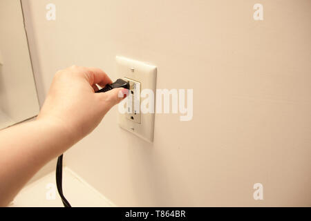 Hand plugs an electrical cord into an outlet at home Stock Photo