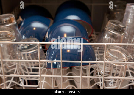 A top rack on a dishwasher with blue bowls and clear glasses Stock Photo