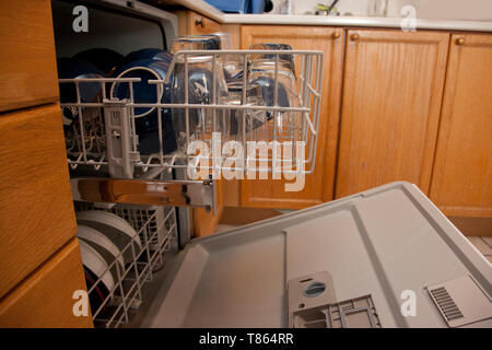 The top drawer of a dishwasher is full of bowls and glassware, in a home or apartment with wood cupboards Stock Photo
