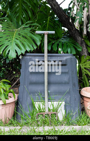 A compost bin and pitch fork in an Australian backyard garden, surrounded by plants and green grass Stock Photo