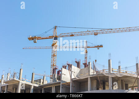unfinished building with cranes on construction site against blue sky Stock Photo