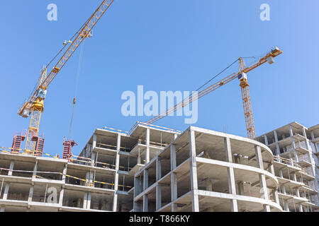 building tower cranes near apartment building under construction against blue sky background. bottom view Stock Photo