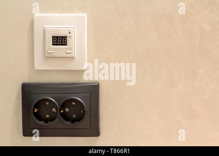 Double electric isolated socket and thermostat installed on light yellow plastered wall. Power supply and temperature regulation, energy saving, comfo Stock Photo
