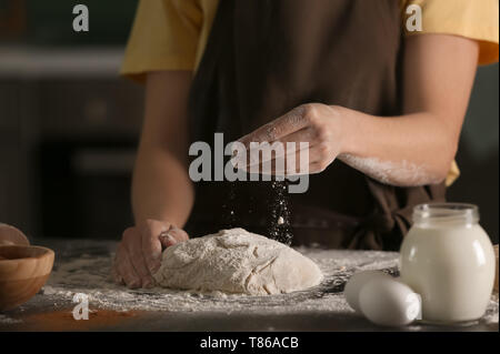 Woman sprinkling dough with flour on kitchen table Stock Photo