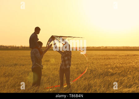 Happy family flying kite in the field at sunset Stock Photo