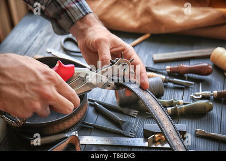 Man using leather punch while working with belt at factory, closeup Stock Photo