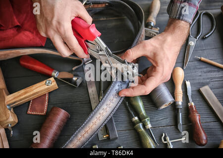 Man using leather punch while working with belt at factory, closeup Stock Photo