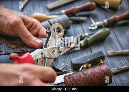 Man using leather punch while working with belt at factory, closeup Stock Photo