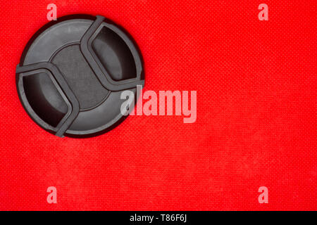 Close up of a black circle lens cap top left corner for DSLR camera lens on a rich red background. Stock Photo