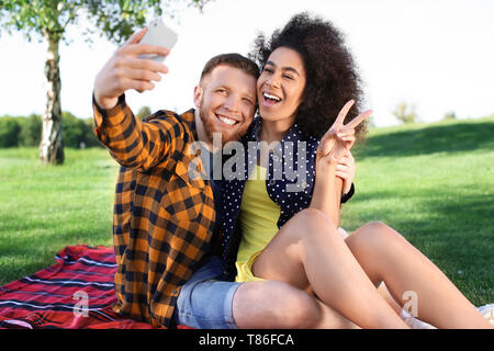 Young loving interracial couple taking selfie outdoors on spring day Stock Photo